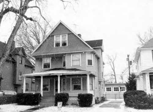 A large, two-story house with a porch, surrounded by snow, in a residential neighborhood.