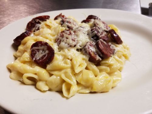 A plate of creamy pasta topped with sliced sausage and melted cheese.