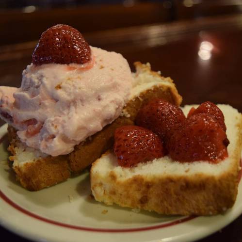 A slice of cake topped with strawberry ice cream and fresh strawberries, served on a plate.
