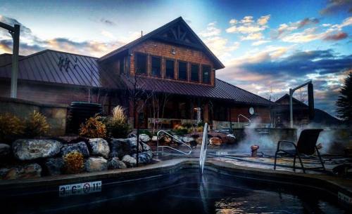 A cozy lodge with a metal roof, surrounded by steam rising from a hot tub, under a colorful sky at dusk.