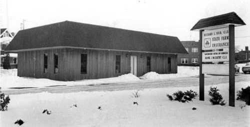 Black and white photo of a single-story building with a sign for State Farm Insurance, surrounded by snow.