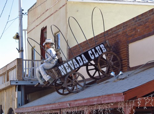A cowboy figure sits on a wooden cart atop a building, with a sign reading "Nevada Club."