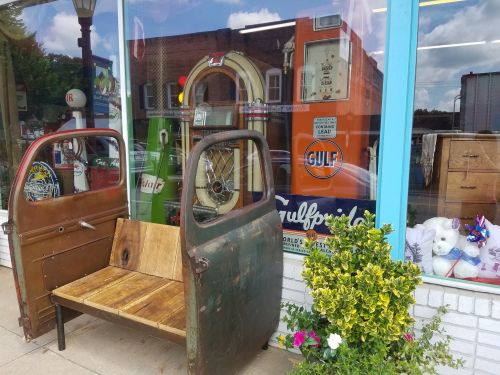A vintage storefront featuring old gas pumps, a wooden bench made from car doors, and colorful decorations.