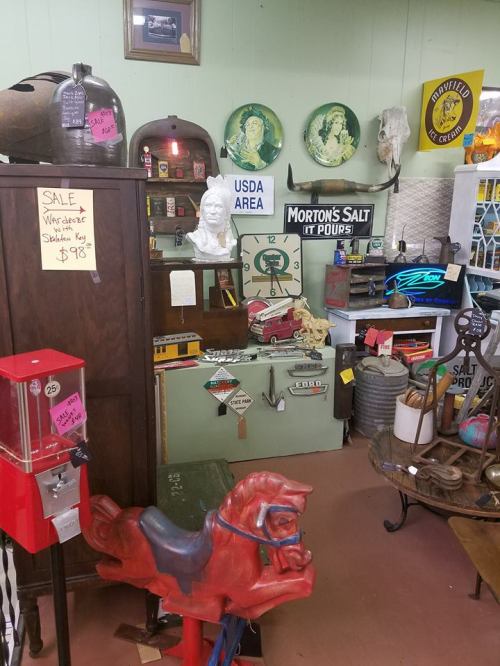A vintage shop filled with antiques, including a red horse ride, signs, and various collectibles on display.