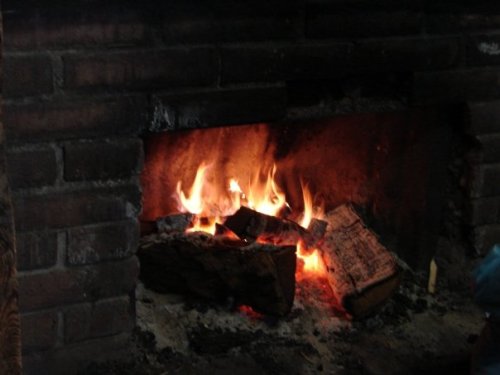 A cozy fireplace with crackling flames and glowing logs, set against a rustic brick backdrop.