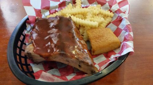 A plate with BBQ ribs covered in sauce, crinkle-cut fries, and a piece of cornbread, all in a checkered basket.