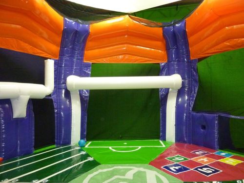 An inflatable play area with colorful walls, a soccer field design, and a large open space for activities.