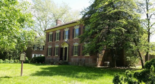 Historic brick house surrounded by greenery, featuring large windows and a welcoming entrance.