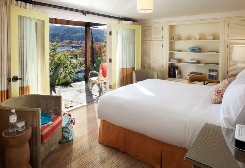 Bright hotel room with a large bed, seating area, and sliding doors opening to a scenic outdoor view.