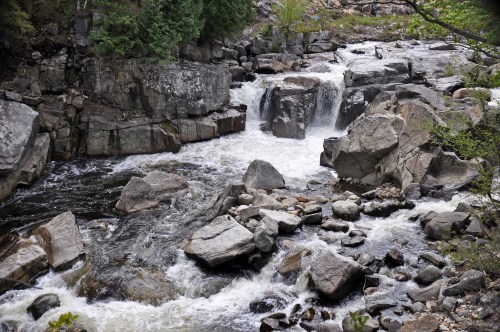 A flowing river cascades over rocks, surrounded by lush greenery and rugged terrain.