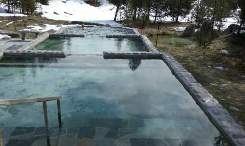 A serene outdoor hot spring pool surrounded by snow-covered ground and trees, with a person relaxing in the water.