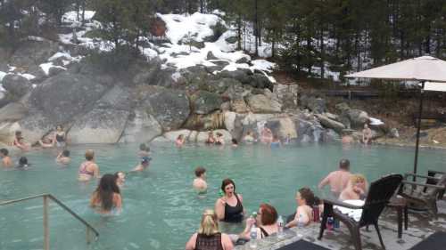 People relax in a steaming hot spring surrounded by rocks and snow-covered trees.