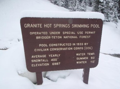 Sign for Granite Hot Springs Swimming Pool, detailing its history, average weather, and water temperatures, surrounded by snow.