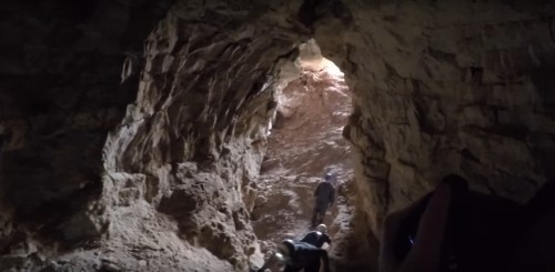 A person climbs through a rocky cave, with light shining in from the opening above.