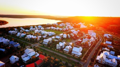 Aerial view of a suburban neighborhood at sunset, with white houses and a lake in the background.