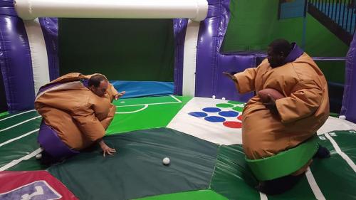 Two people in inflatable sumo suits play on a colorful, inflatable sports-themed arena.