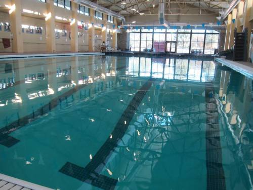 Indoor swimming pool with clear water, reflections, and large windows letting in natural light.