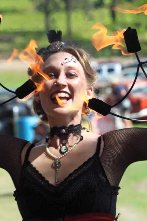 A performer joyfully spins flaming poi, showcasing a vibrant smile and intricate costume at an outdoor event.