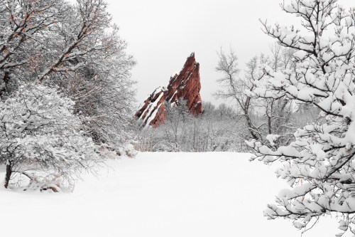 Snow-covered landscape with trees and a prominent red rock formation in the background.