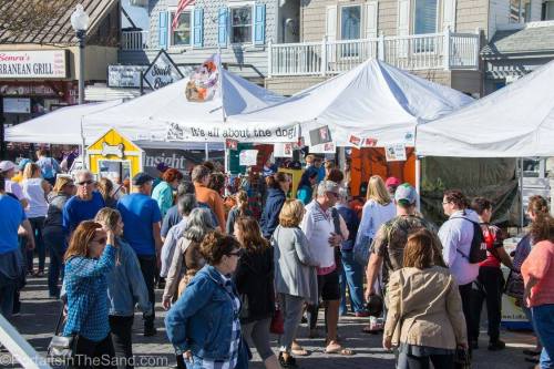 A bustling outdoor market with people browsing tents and stalls, enjoying a sunny day.