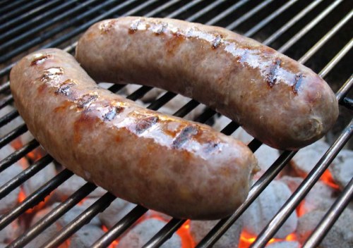 Two grilled sausages sizzling on a barbecue grill over glowing charcoal.