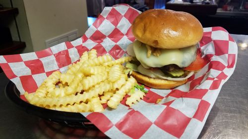 A juicy burger with cheese, lettuce, tomato, and pickles, served with a side of crinkle-cut fries on a checkered paper.