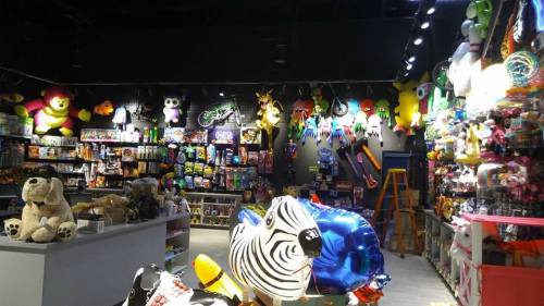 A colorful store interior filled with toys, plush animals, and decorations, with shelves and a ladder in the background.