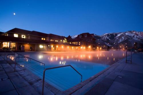 A serene outdoor pool at dusk, surrounded by mountains and softly lit buildings, creating a tranquil atmosphere.