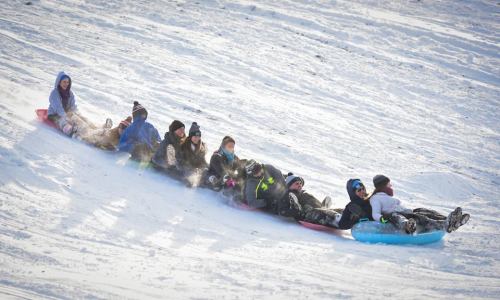 A group of people sledding down a snowy hill, enjoying a fun winter day together.