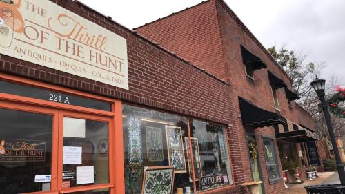 Exterior of a brick building featuring a sign for "The Thrill of the Hunt" antique shop, with awnings and decorative windows.