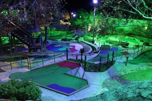 A brightly lit mini-golf course at night, featuring colorful holes and lush greenery under green and purple lights.