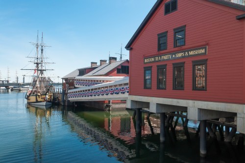 Historic Boston Tea Party Ships and Museum with a ship docked, reflecting in calm waters under a clear blue sky.