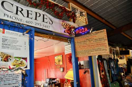 A colorful food stall featuring a crepes sign and a pizza menu, decorated with lights and festive elements.