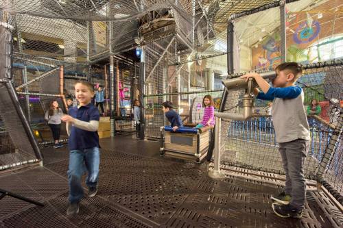 Children play in a colorful indoor playground with climbing structures and interactive features.
