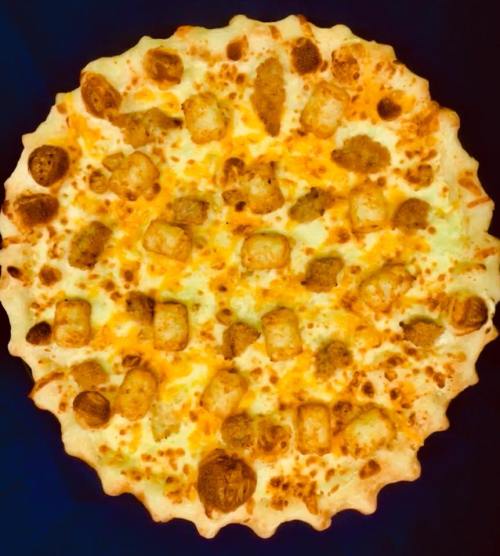 A round pizza topped with golden cheese and small, crispy potato bites on a golden crust.