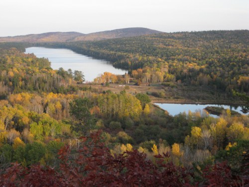A scenic view of a river winding through autumn-colored trees and hills, reflecting the vibrant foliage.