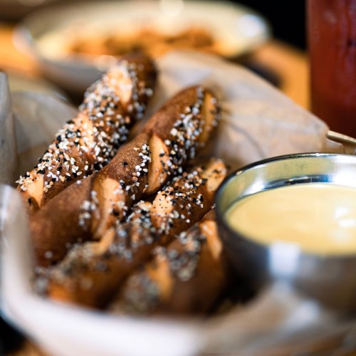 A basket of pretzel twists sprinkled with salt, served with a small bowl of cheese dip.