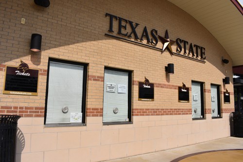 Ticket booth exterior at Texas State, featuring multiple windows and a sign with the website.
