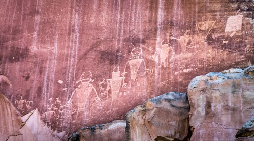 Ancient rock art depicting humanoid figures with helmets, etched into a reddish stone surface.