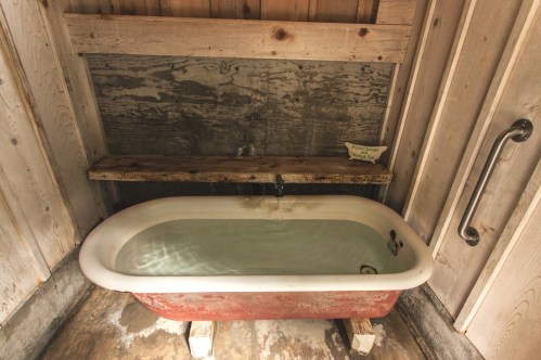 A vintage bathtub with water, set against rustic wooden walls and a wooden shelf above.