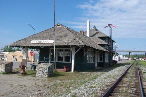 Historic Nenana train station with a wooden structure, surrounded by tracks and a clear blue sky.