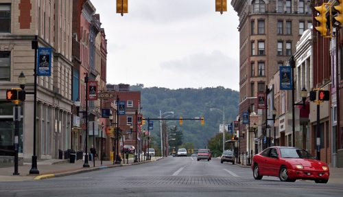 A quiet downtown street with historic buildings, traffic lights, and a few cars under a cloudy sky.