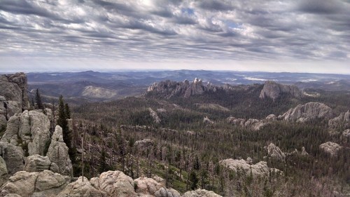 A panoramic view of rugged mountains and dense forests under a cloudy sky.