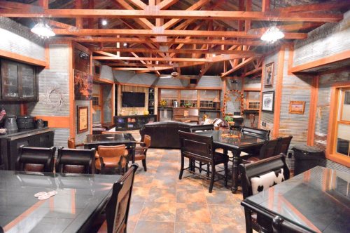 A spacious, rustic-style interior with wooden beams, dining tables, and a cozy seating area.