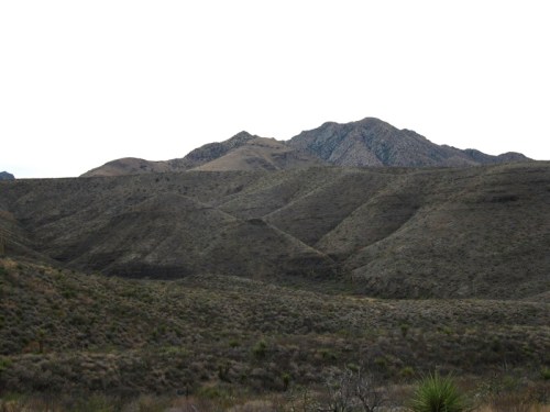 A rugged landscape featuring rolling hills and distant mountains under a cloudy sky.