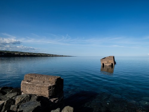 A calm lake scene with clear blue skies and a partially submerged stone structure in the water.