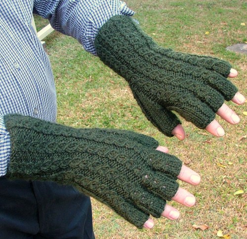 A person wearing green knitted fingerless gloves, showing hands against a grassy background.