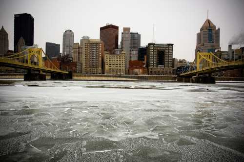 A frozen river with ice formations in the foreground, city skyline and bridges in the background on a cloudy day.