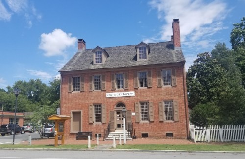 Historic Cantwell's Tavern, a two-story brick building with a gabled roof, surrounded by trees and a clear blue sky.