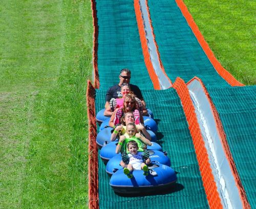 A group of people enjoying a fun ride down a grassy slope on inflatable tubes, smiling and having a great time.